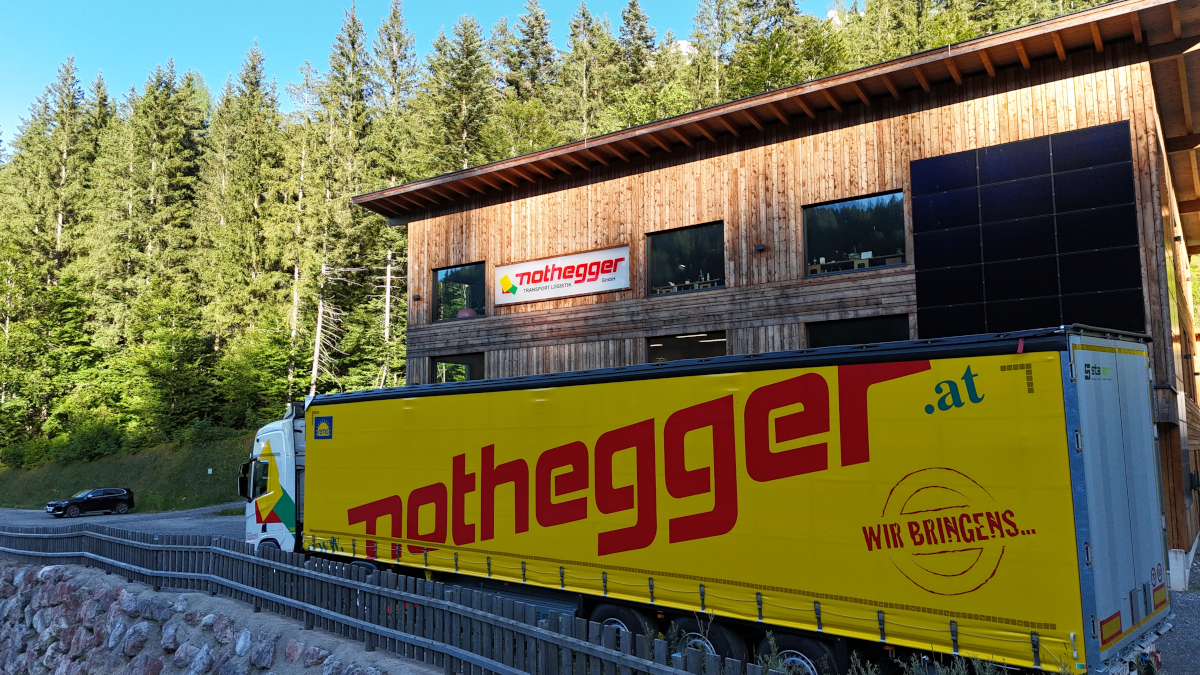 Sattelzug mit gelber Plane und Nothegger Schriftzug steht vor der Firmenzentrale, einem modernen Holzgebäude ebenfalls mit Nothegger Schriftzug in St. Ulrich am Pillersee